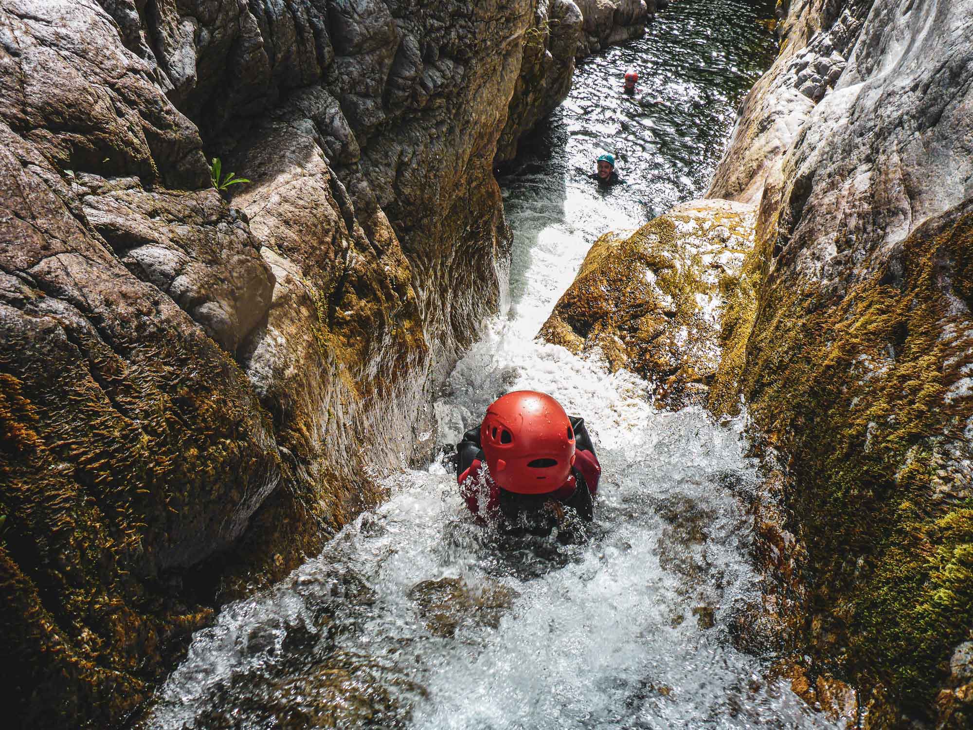 Un enfant glissant dans un toboggan naturel étroit sur le parcours canyoning demi-journée Azéro avec Nature Canyon Ardèche